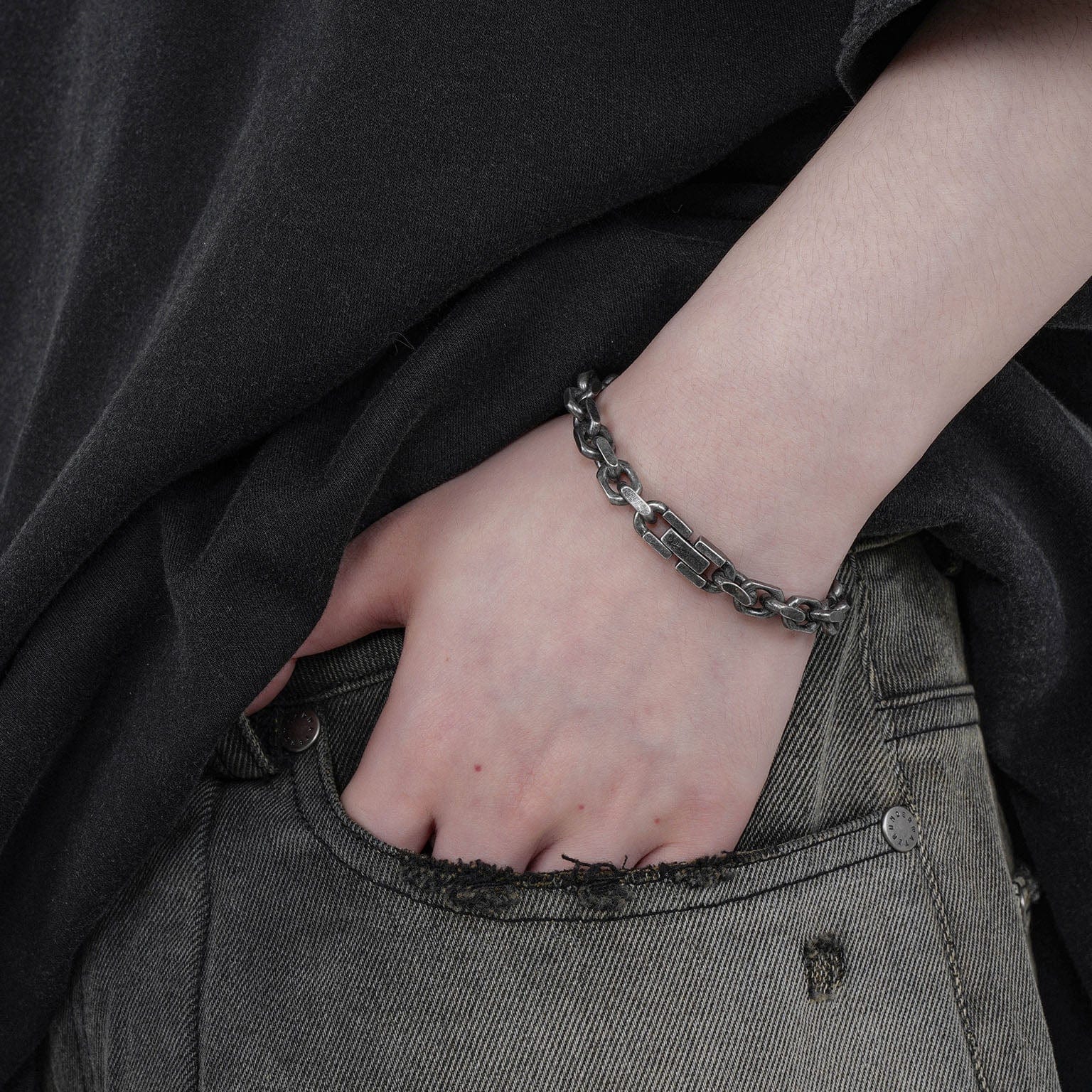 Person wearing a chain bracelet on a plain background