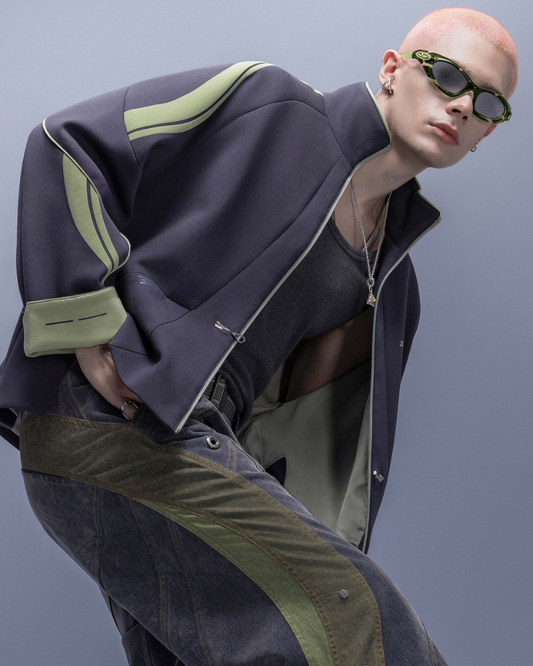 Person wearing a dark jacket with green accents and sunglasses on a plain background