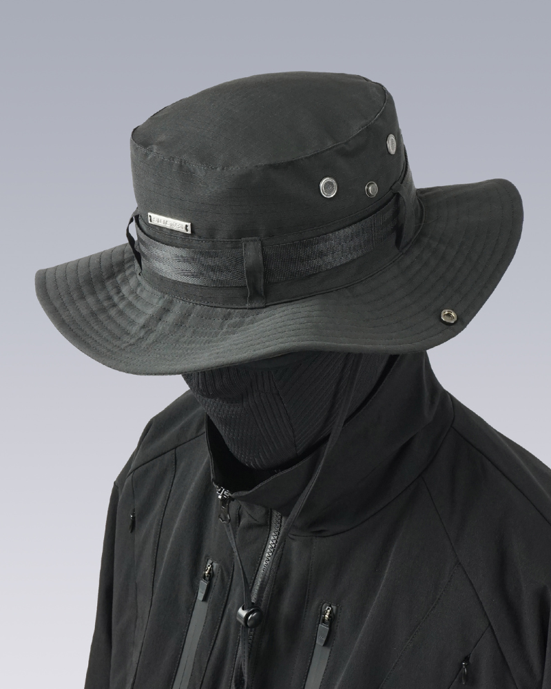 Person wearing a black wide-brimmed techwear hat with a brand logo on a light gray background