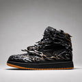 A single high-top sneaker shown in profile against a neutral gray studio background. The shoe is predominantly black with metallic bronze and gold dragon-like sculpted overlays and a gum brown outsole.