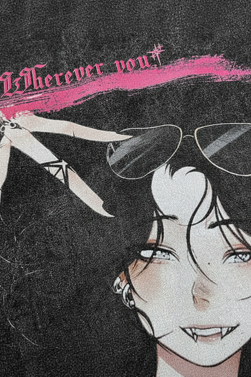 Close-up of a graphic print featuring an illustrated anime-style face with dark hair, sunglasses, and a pink brushstroke accent with gothic text at the top.
