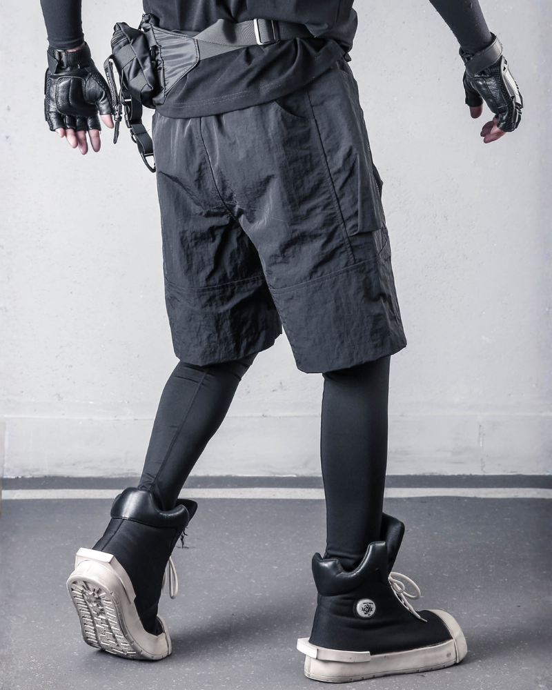 Person wearing dark cargo shorts, black gloves, and high-top sneakers on a gray floor.