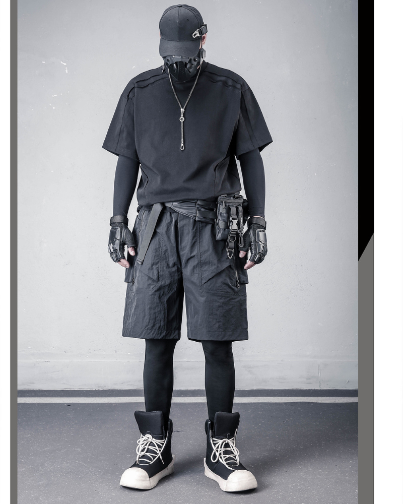 Person wearing a black outfit with tactical gear against a gray wall.