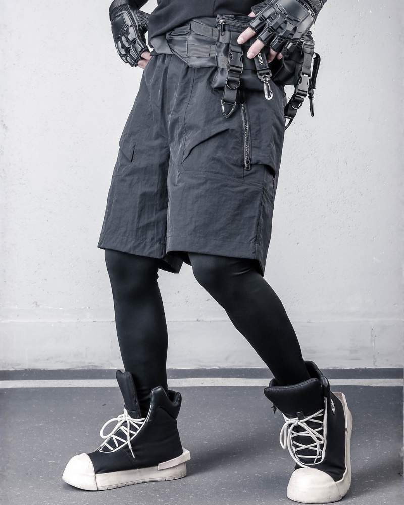 Person wearing tactical shorts, gloves, and boots against a gray background