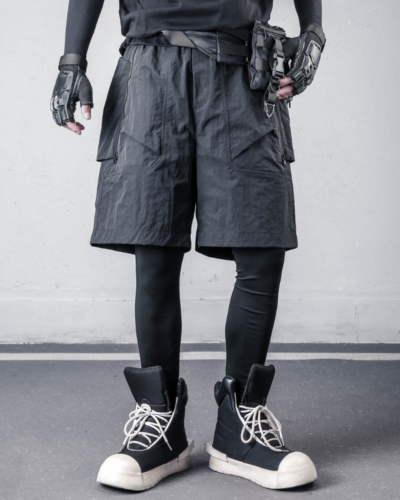 Person wearing dark tactical shorts, gloves, and high-top sneakers on a plain background
