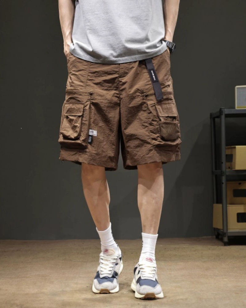 Person wearing brown cargo shorts with a gray shirt and white sneakers in a room.