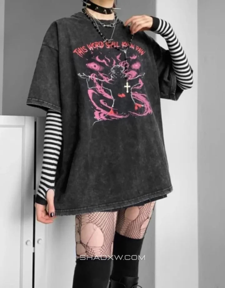 A person wearing an oversized faded black graphic T-shirt with pink gothic-style artwork and text, layered over a black-and-white striped long-sleeve shirt, with fishnet tights and black boots in a room setting.