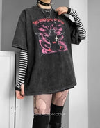 A person wearing an oversized faded black graphic T-shirt with pink gothic-style artwork and text, layered over a black-and-white striped long-sleeve shirt, with fishnet tights and black boots in a room setting.