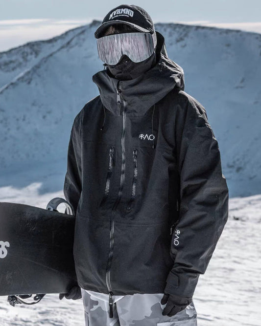 Person in black snow jacket and goggles holding a snowboard on a snowy mountain