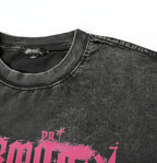 Close-up of a washed black t-shirt showing the collar, textured fabric, and a pink graphic print with the brand name 'SHADOW' on the front.