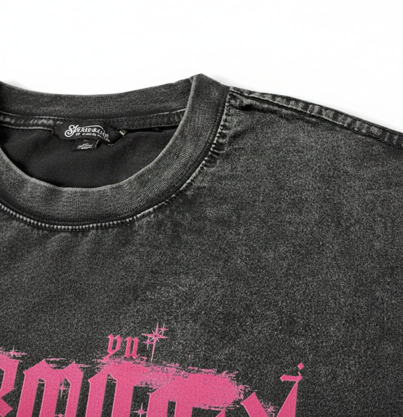 Close-up of a washed black t-shirt showing the collar, textured fabric, and a pink graphic print with the brand name 'SHADOW' on the front.