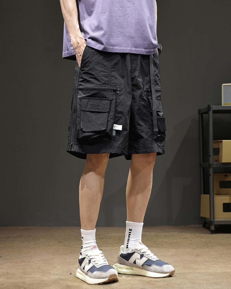 Person wearing black cargo shorts with multiple pockets, a purple shirt, white socks, and sneakers on a dark background.