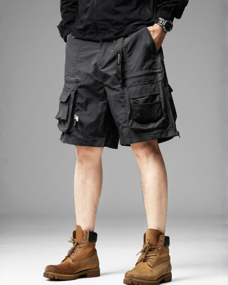 Person wearing black cargo shorts and brown boots on a gray background