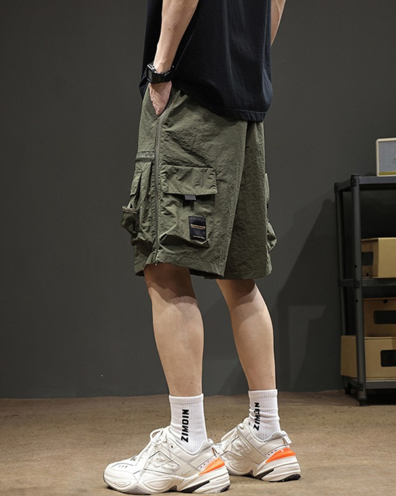 Person wearing green cargo shorts and white sneakers in a room with a dark wall.