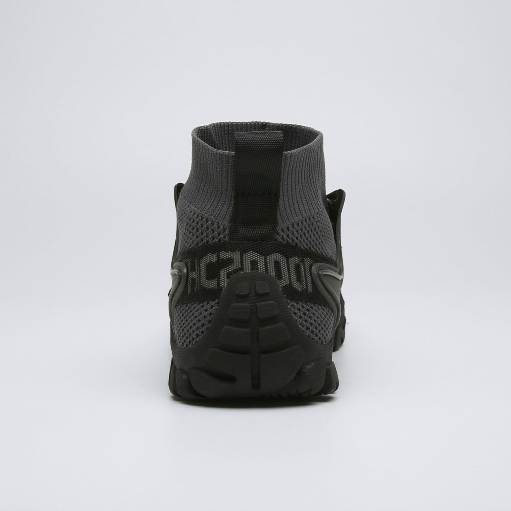 A dark gray and black athletic sock-style sneaker shown from the back, featuring a knit upper, a pull tab, and a chunky black sole with textured detailing.