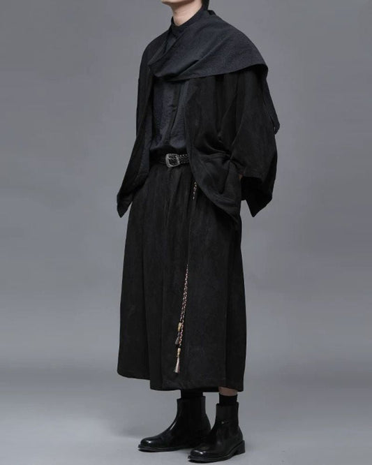 Person wearing a long black coat with a plain background