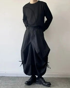 Clotechnow black baggy hakama pants with a wide-leg draped silhouette and side tie details worn with black boots
