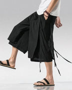 Clotechnow black sarouelle drape hakama pants with wide-leg silhouette and side tie details worn with sandals