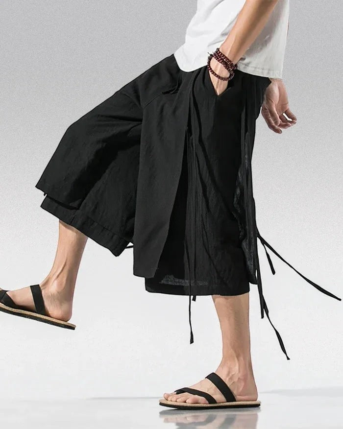 Clotechnow black wide-leg sarouelle hakama pants with draped fabric and tie details worn with sandals
