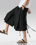 Clotechnow black wide-leg sarouelle hakama pants with draped fabric and tie details worn with sandals