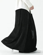 Clotechnow black wide-leg Harajuku hakama pants with a pleated texture and draped silhouette worn with white sneakers.