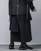 Clotechnow black pleated hakama pants with wide-leg silhouette and tactical strap details worn with dark sneakers.