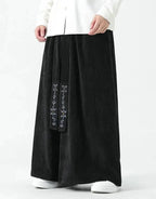 Clotechnow black wide-leg hakama pants with vertical texture and embroidered detailing worn with white sneakers