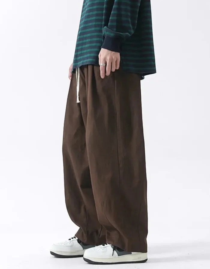 Clotechnow brown wide-leg hakama pants with a drawstring waist, styled with a striped long-sleeve shirt and sneakers.