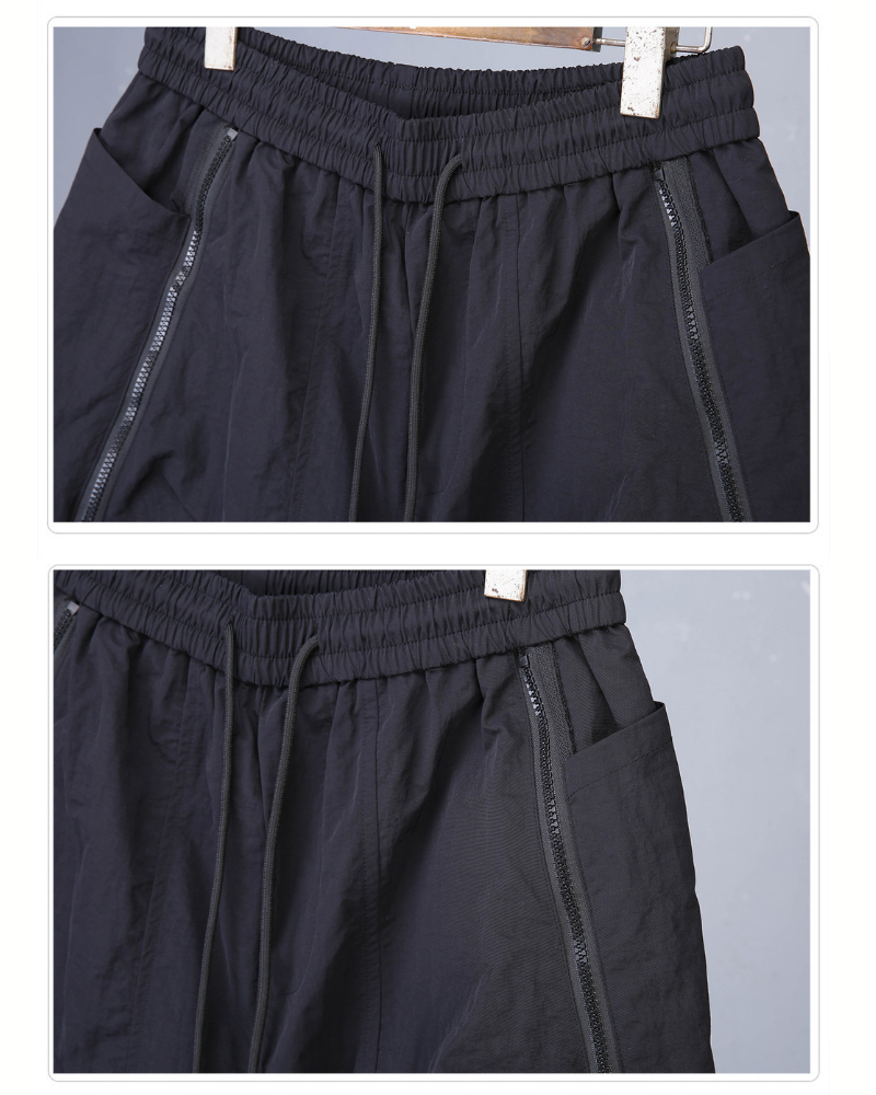 Black pants with drawstring waist and side zippers on a gray background