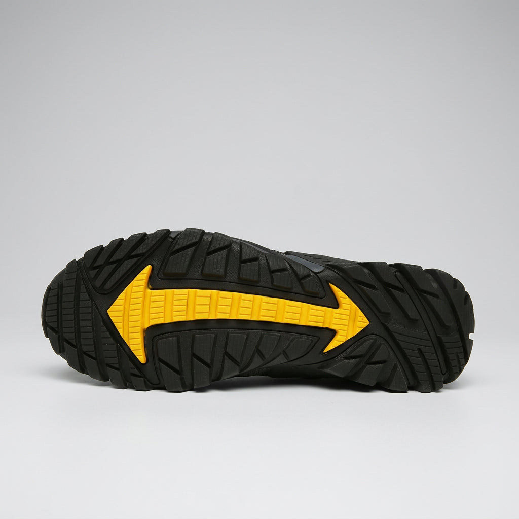 A close-up of a black rugged shoe sole with a bold yellow arrow graphic on the bottom, photographed against a light gray studio background. veloweave high quality techwear shoes