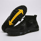 A pair of black athletic ankle boots with a textured knit upper, black laces, and a prominent bright yellow accent on the outsole, shown on a light gray background.